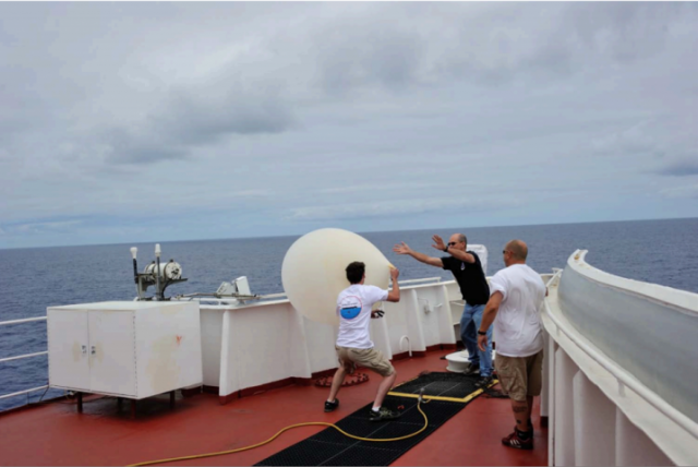 Struggling with a weather balloon on the prow of a ship