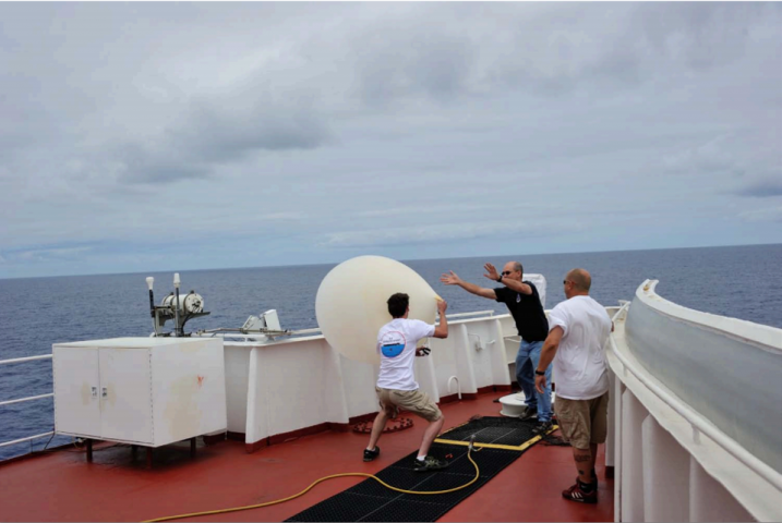 Struggling with a weather balloon on the prow of a ship