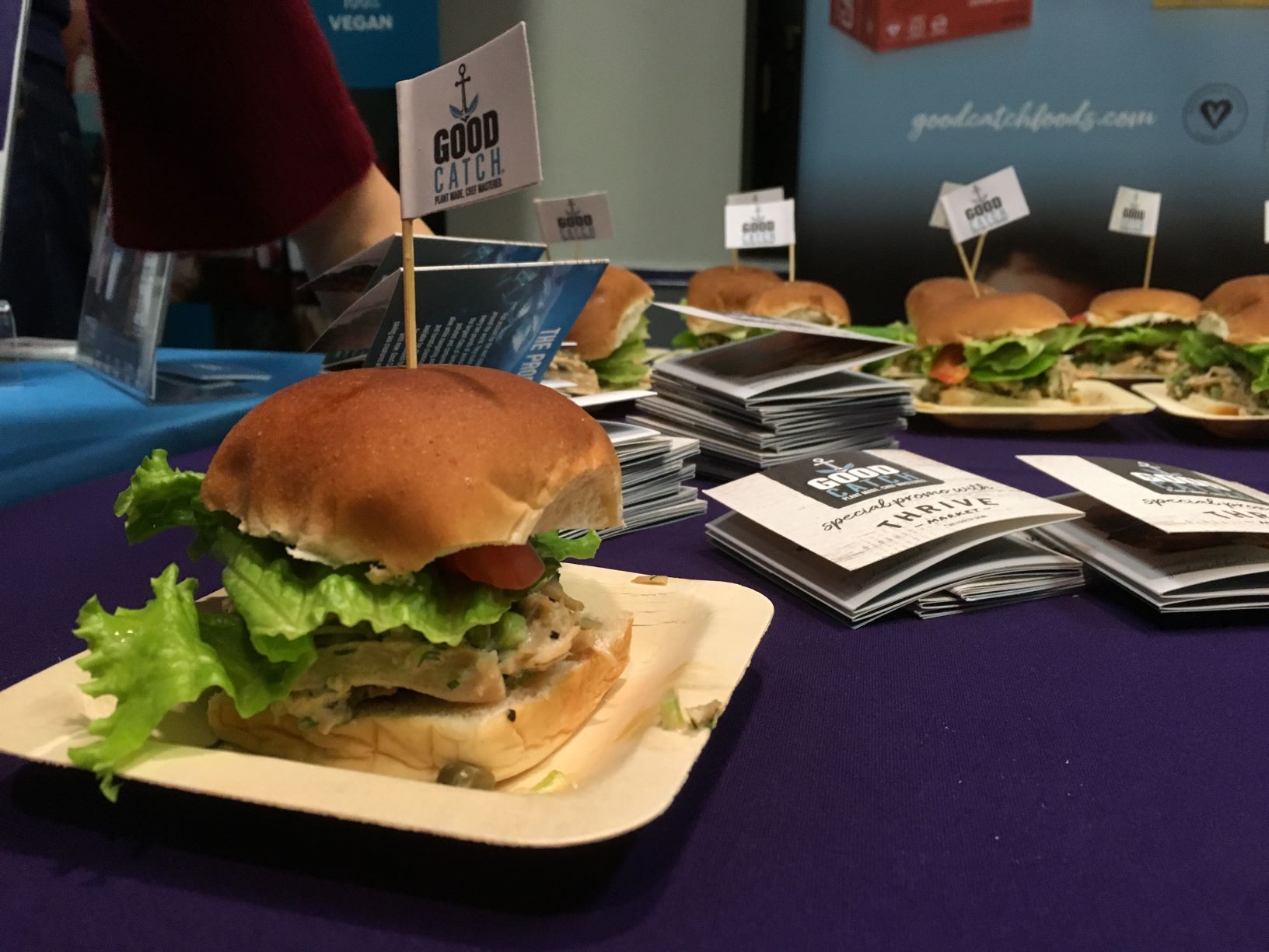 A veggie burger sits on a paper plate on a blue tablecloth.