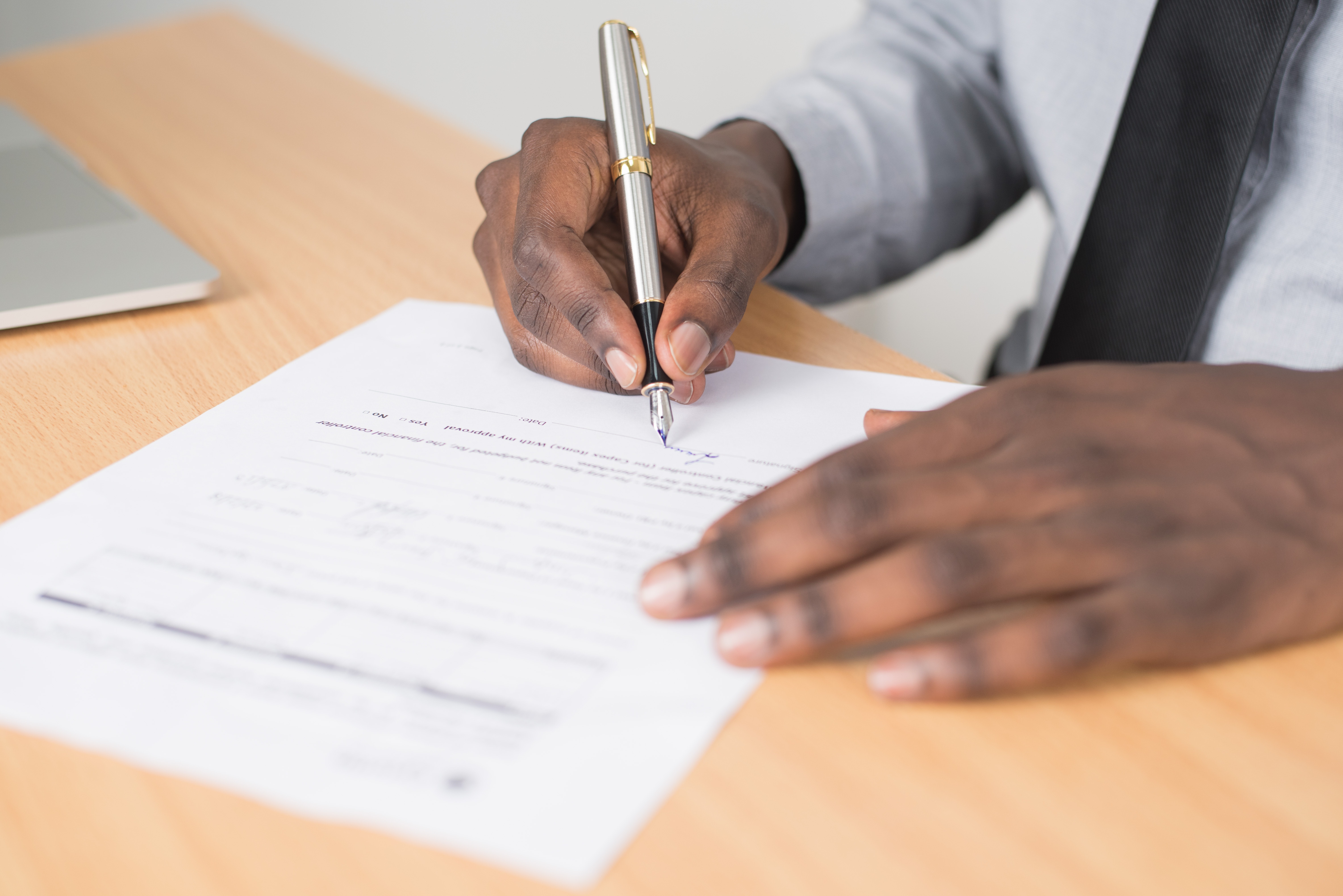 A hand holding a ballpoint pen writes on a document on a desk