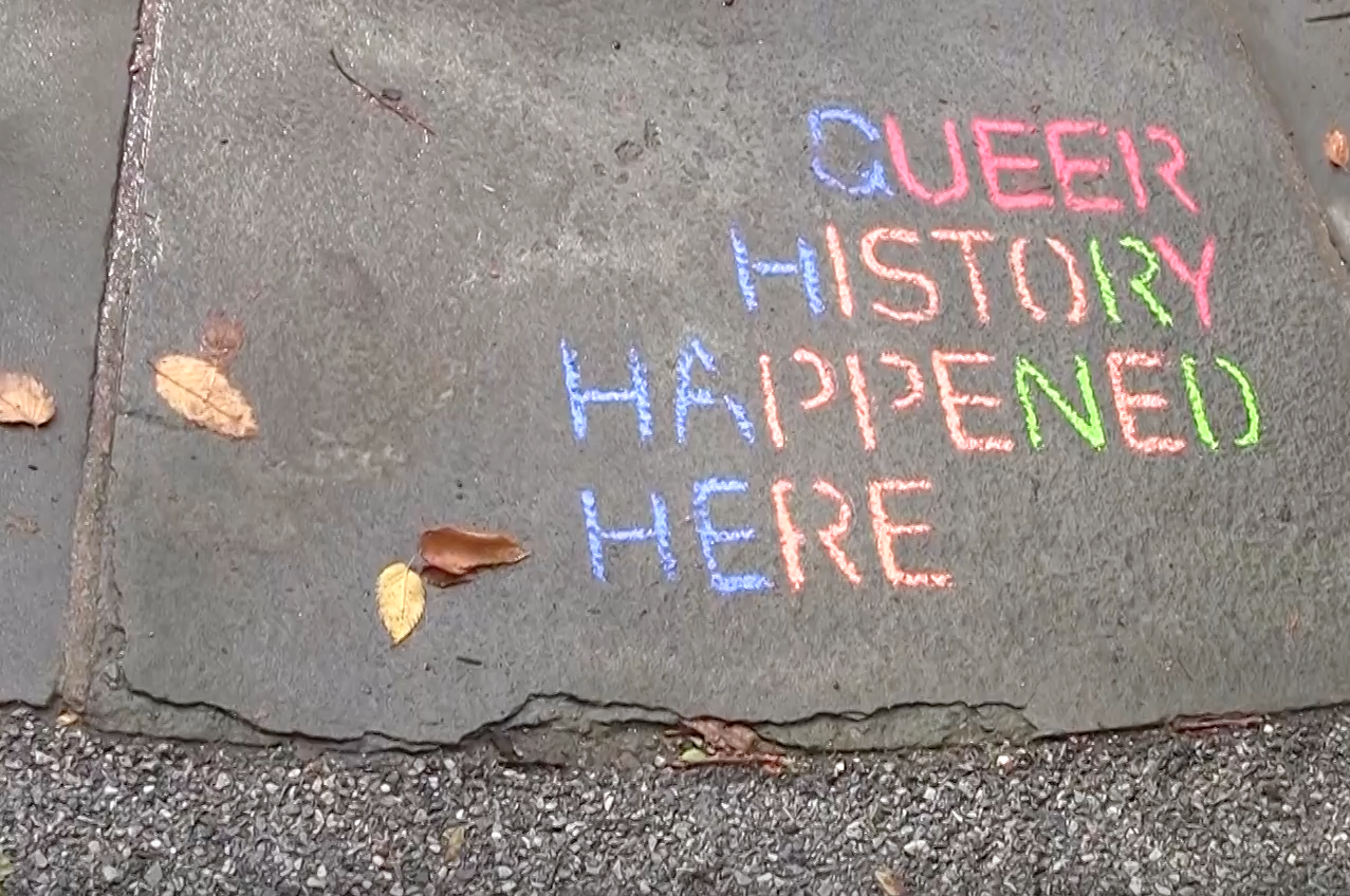 "Queer history happened here," written in chalk on ground.