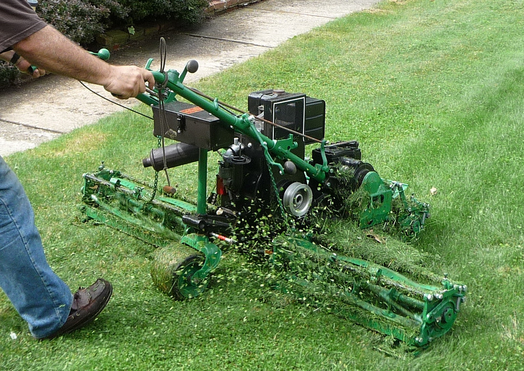 a person pushes lawnmower across grass