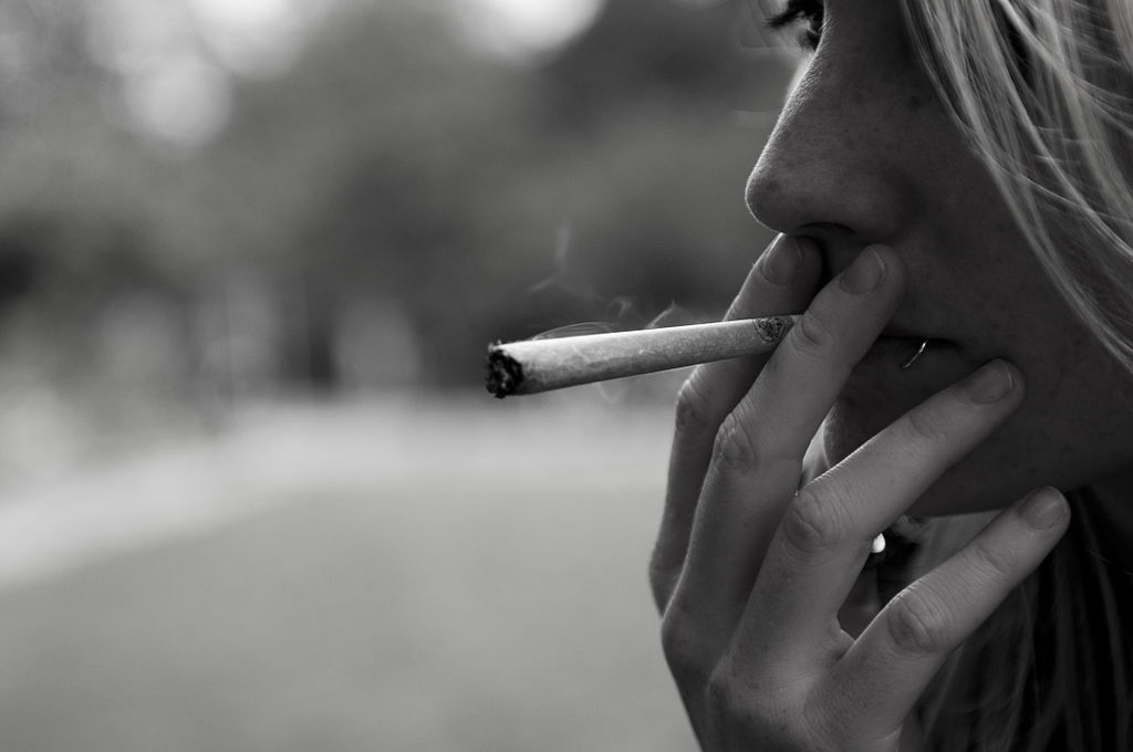 In the right-hand side of the photo, a close-up profile of a blond woman holding a joint to her lips. The photo is in black and white.