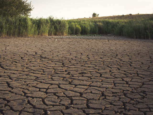 Lake dried out by water scarcity. A mountain with dried plants is on the background.