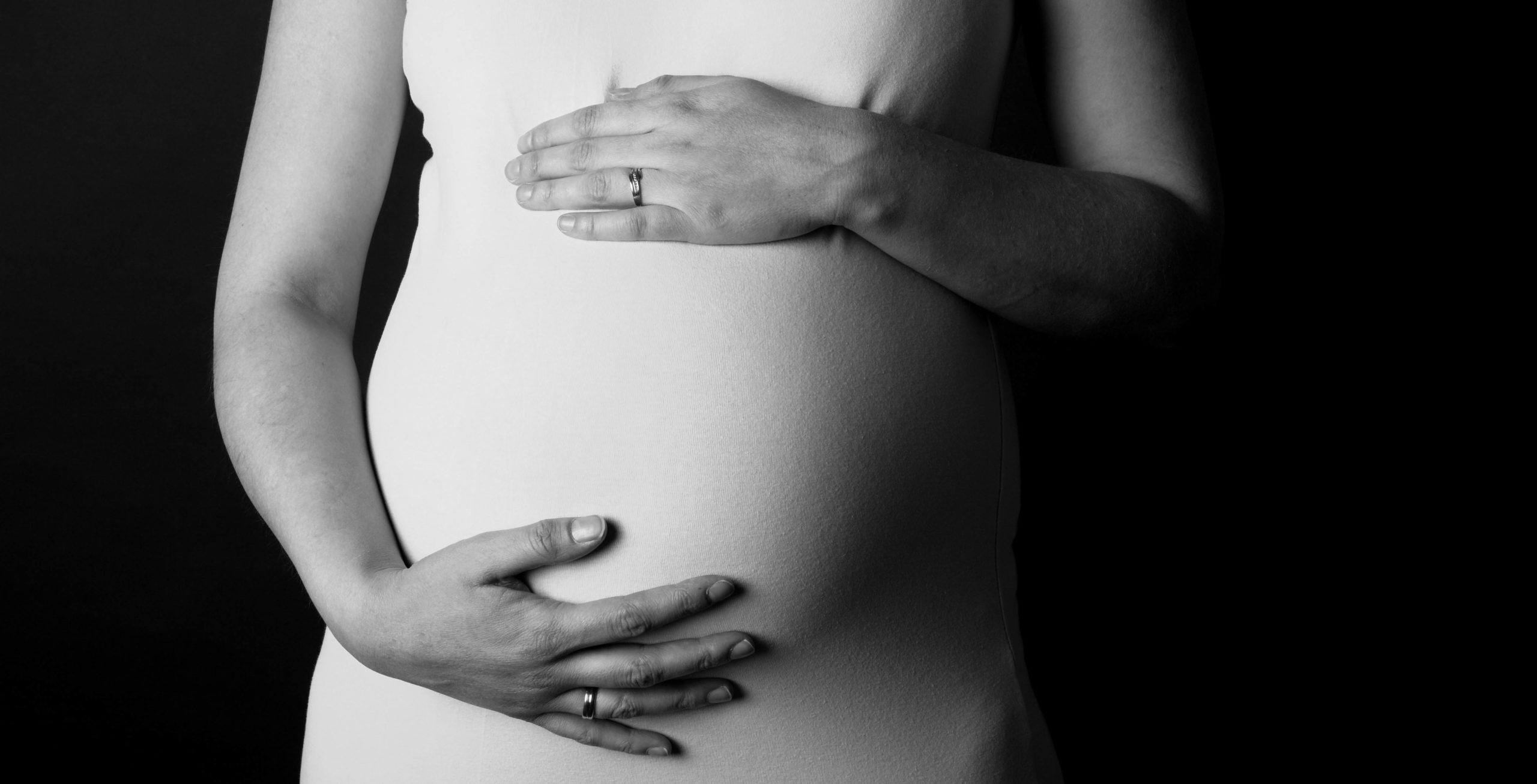 Black and white photo of pregnant woman wearing a white dress