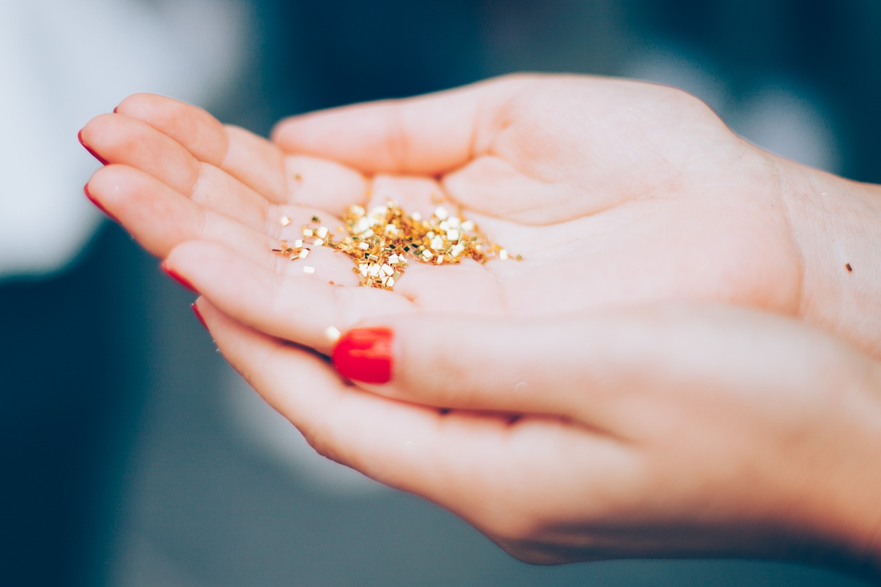 Two hands with red nail polish cupped and holding gold glitter