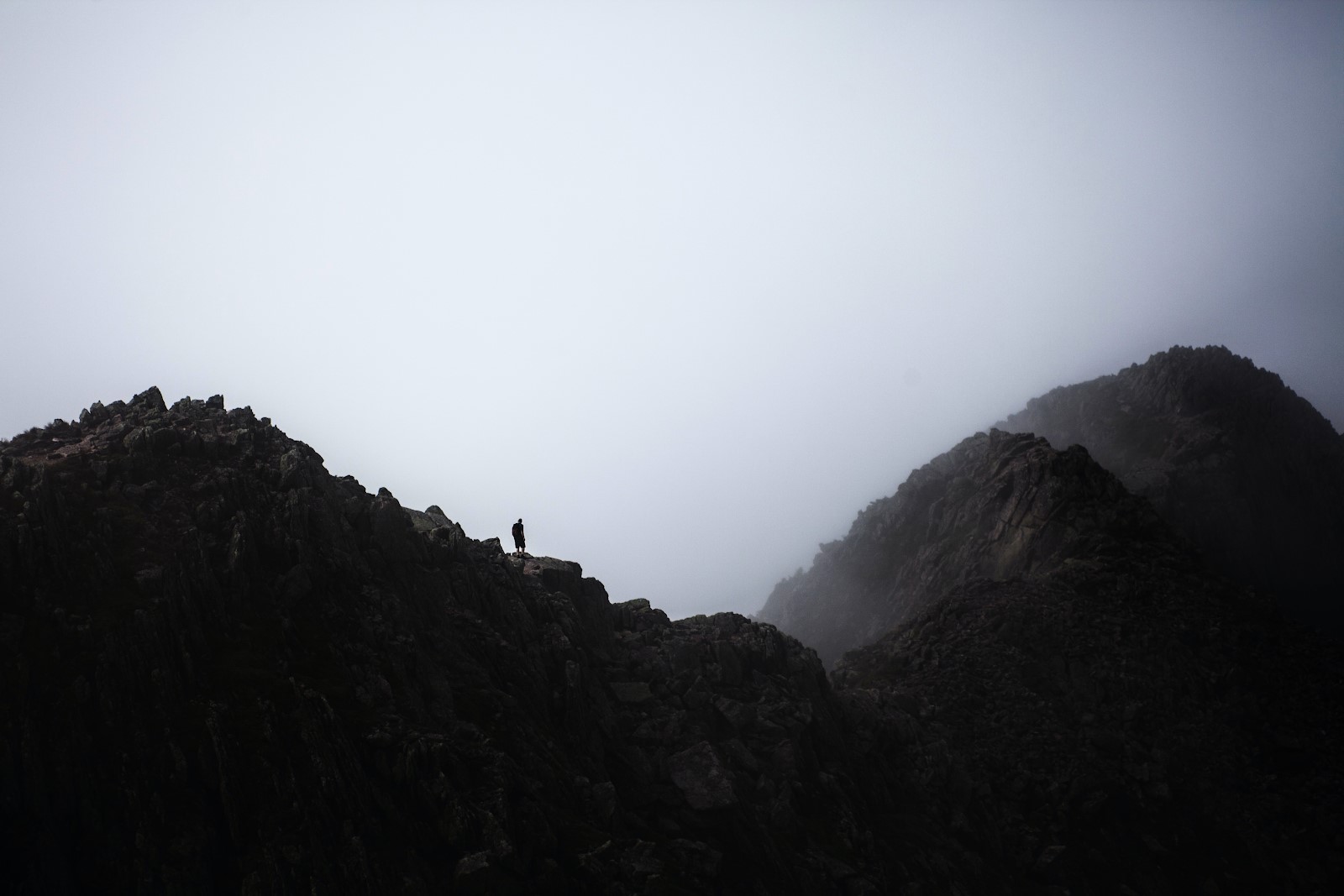 Image of Mount Katahdin in Maine with a lone figure on it silhouetted against a cloudy, misty sky.