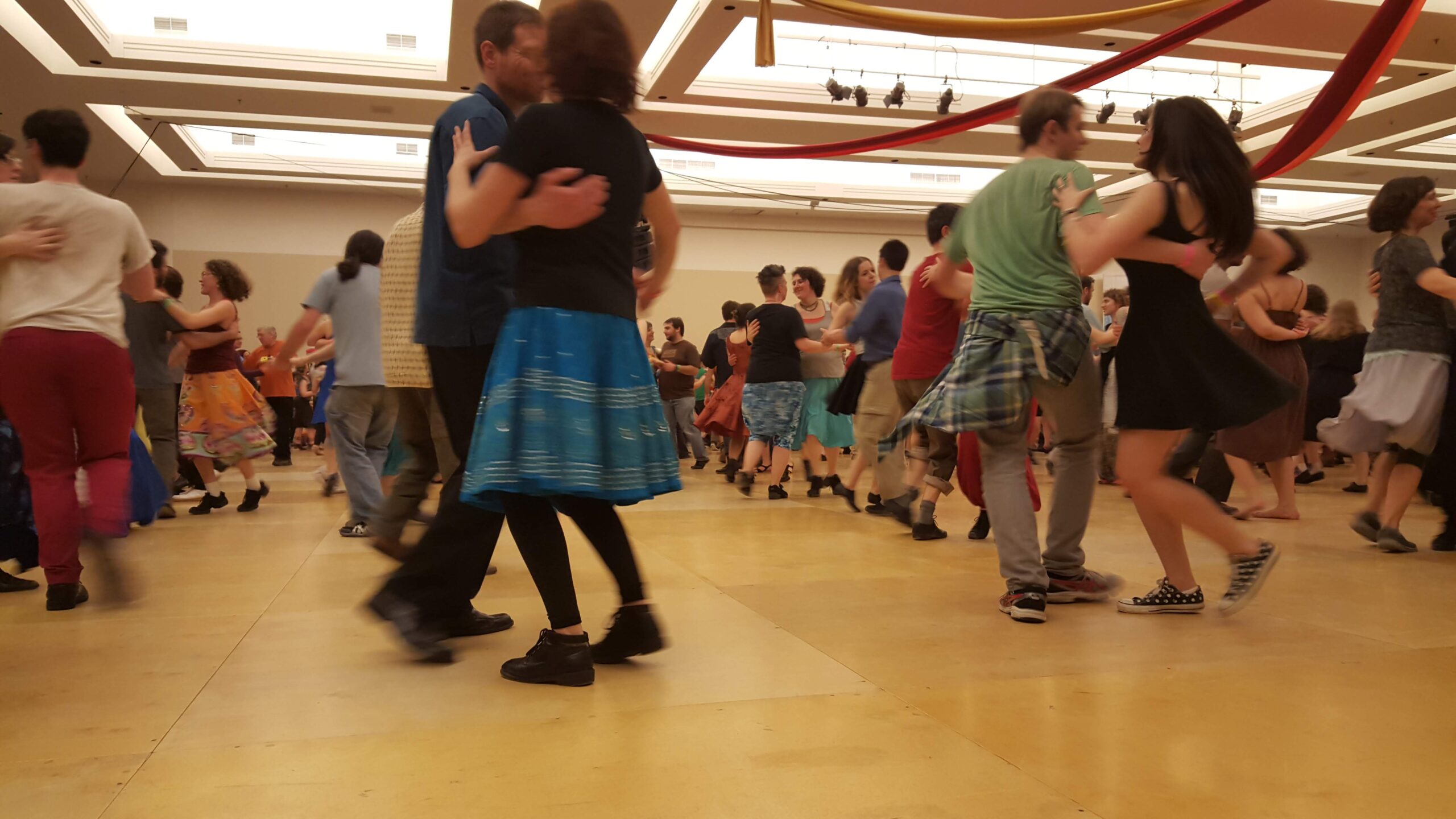 Image of lines of people contra dancing in a large room with wooden floors.