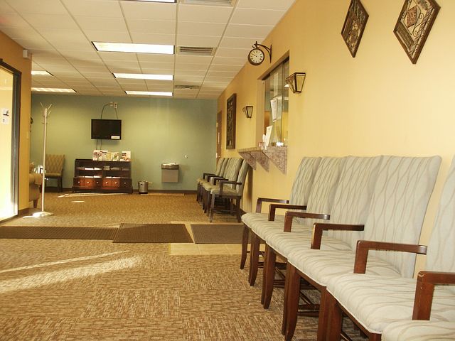 A row of chairs sit empty in a fluorescent lit waiting room.