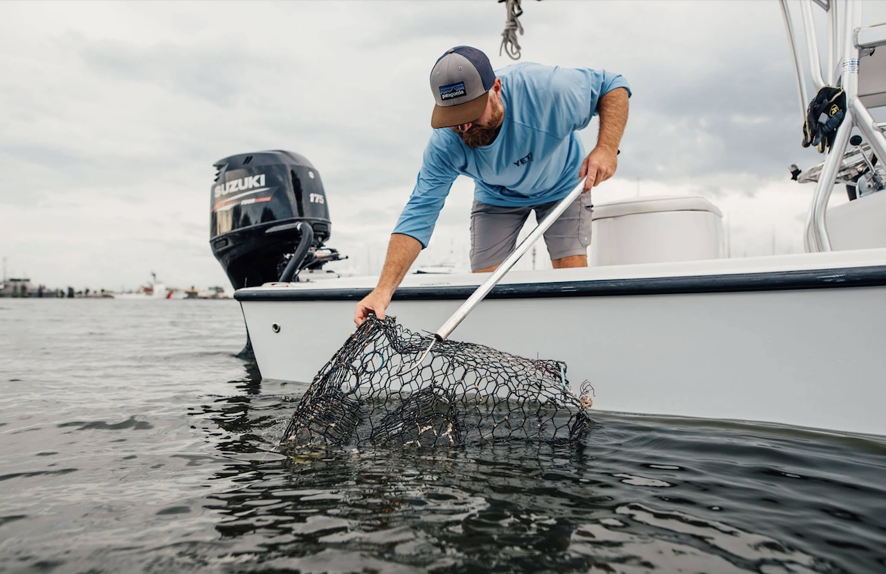 Neill Holland holds a crab trap dipped in water and stands on a white boat