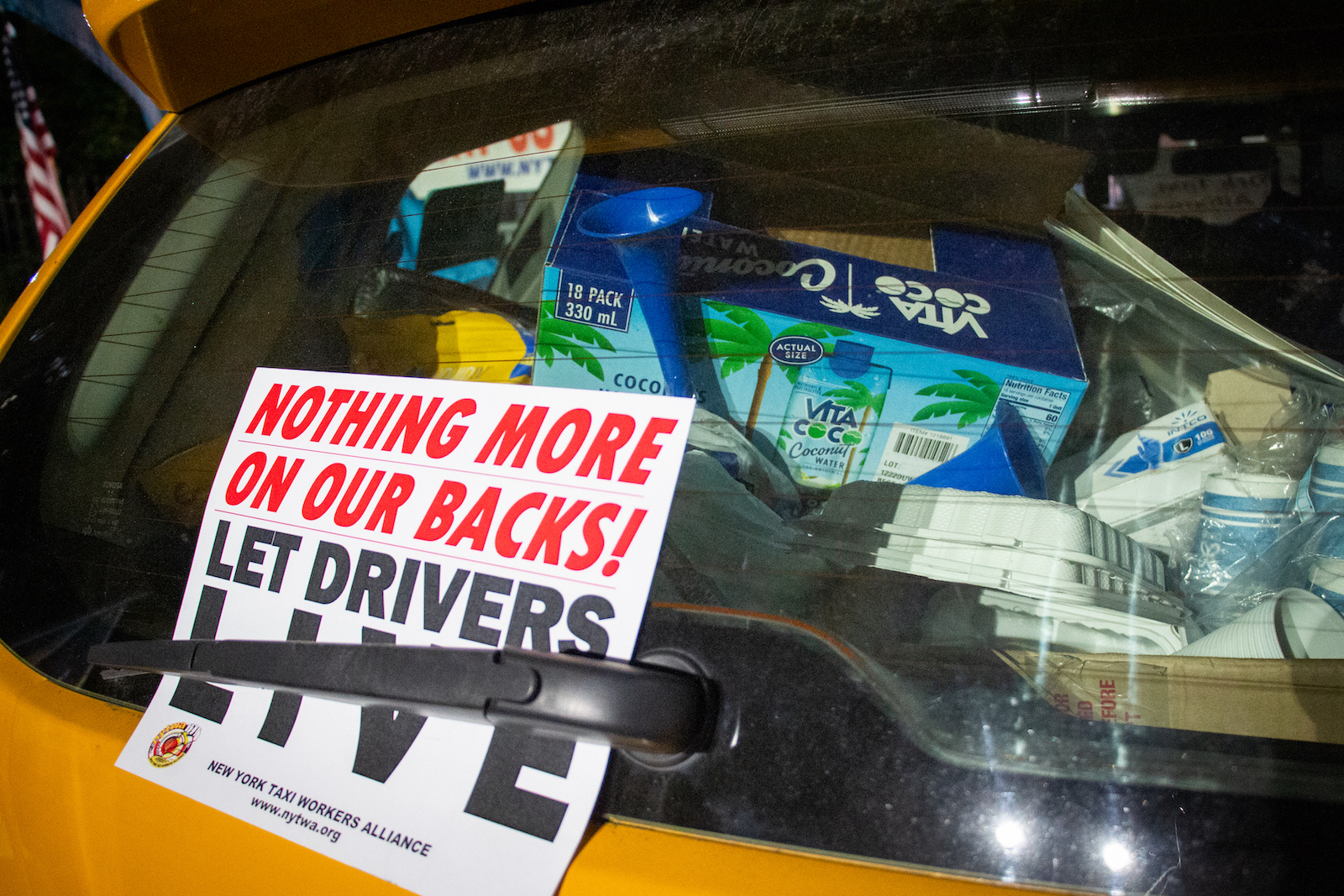 The back of a yellow cab is packed with coconut water, plastic noisemakers, paper cups and other protest supplies. A sign reading "Nothing more on our backs! Let drivers live," is stuck between the back windshield wiper and the glass.