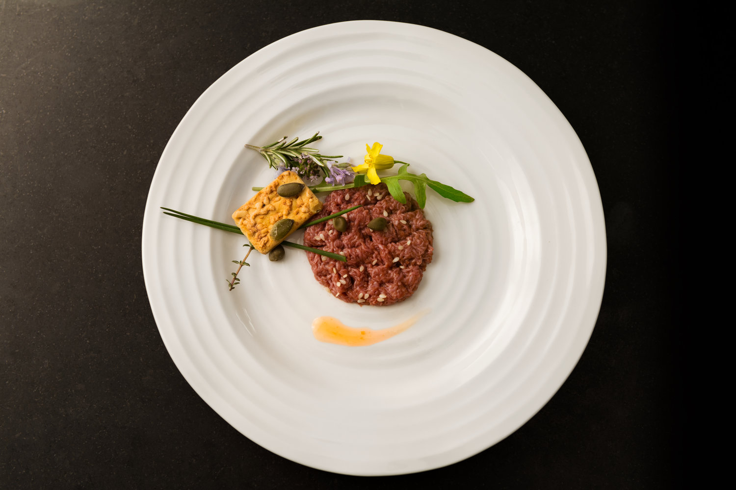 An artfully presented plate of cultured, raw ground beef garnished with greens and a cracker.
