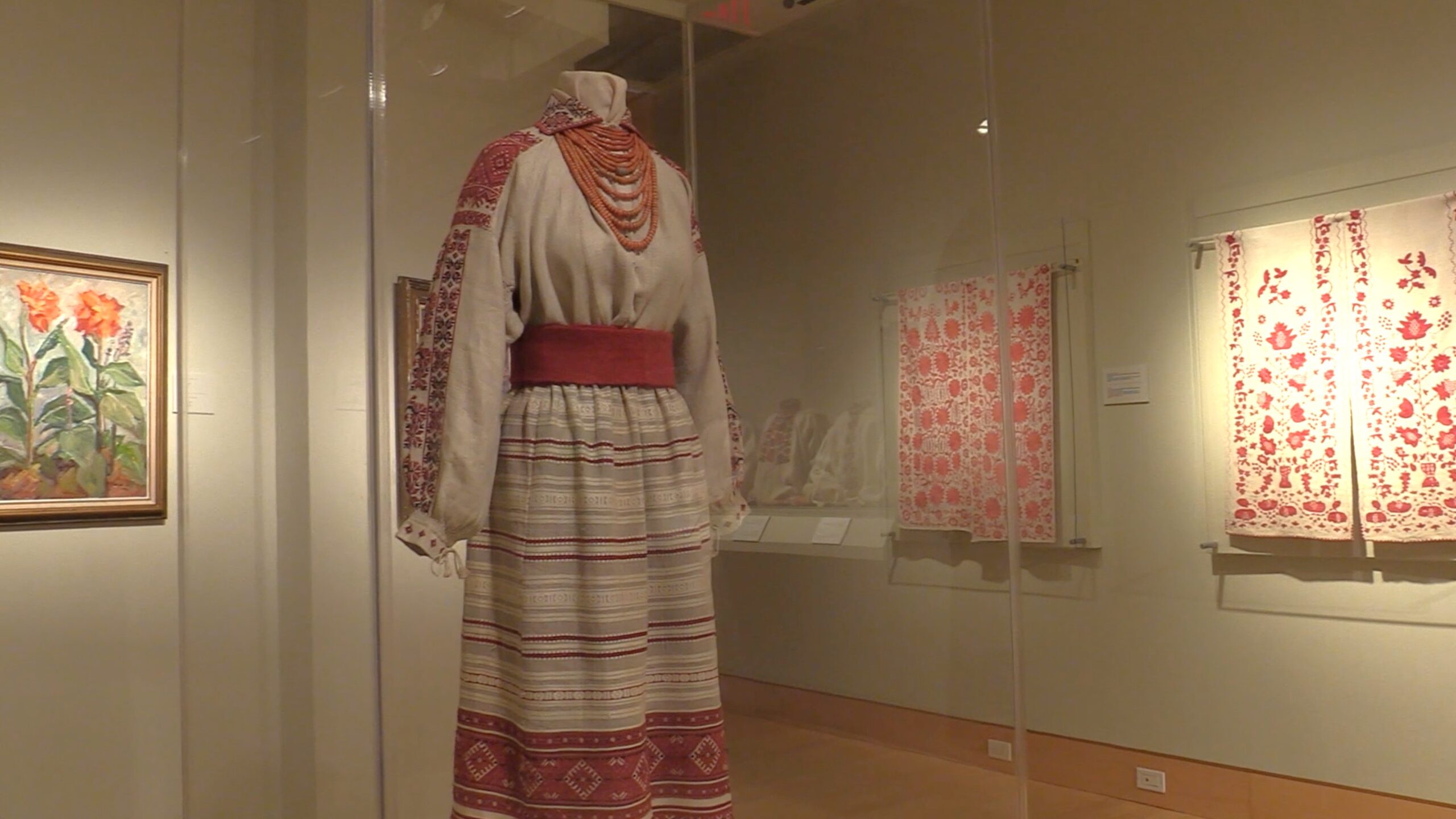 A photograph from inside the Ukrainian Museum; a white-and-red traditional Ukrainian dress stands in the middle, flanked by other Ukrainian artwork hanging on the walls.