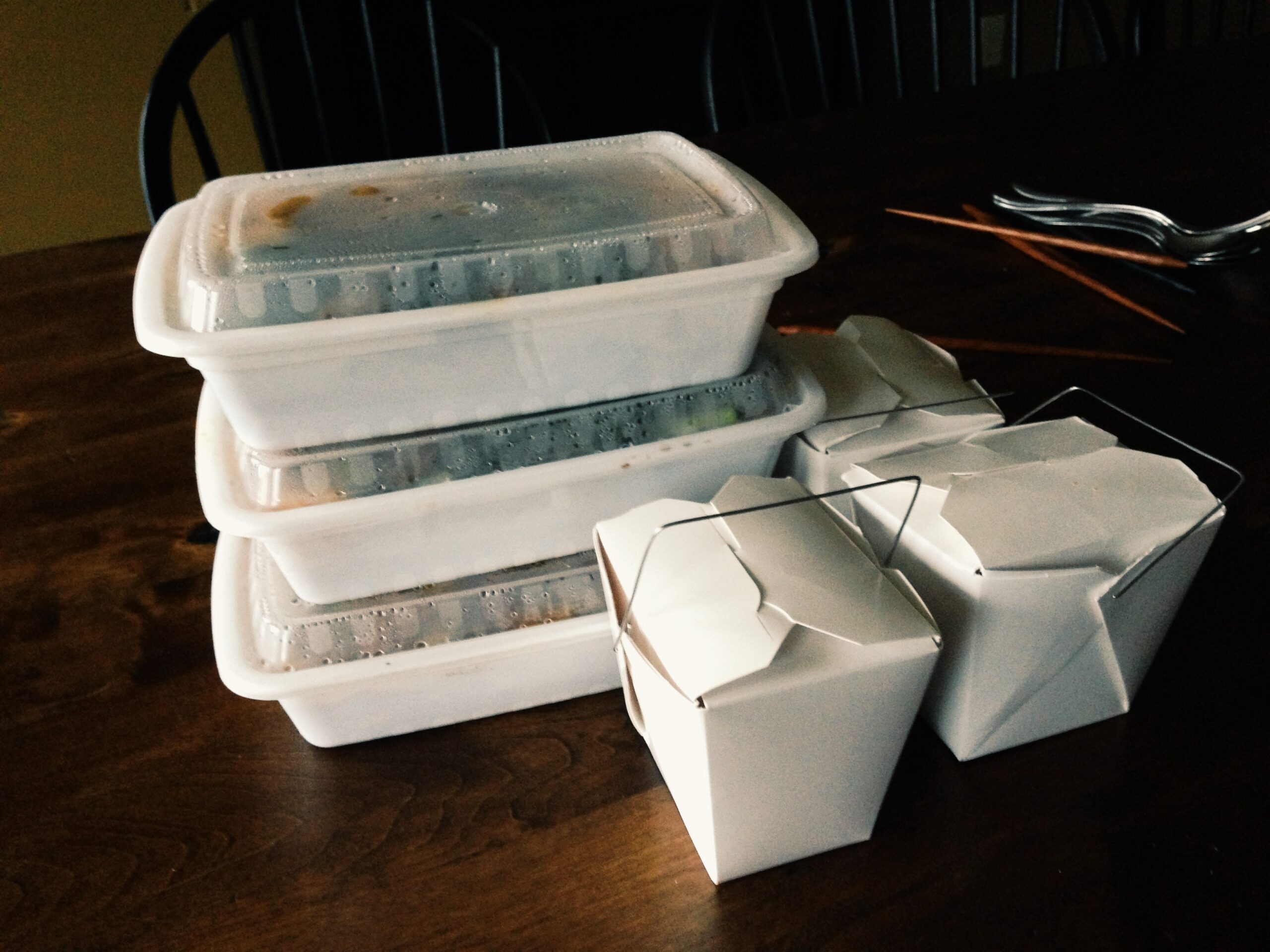 In the foreground there are two plastic takeout rice boxes, behind them a stack of three sturdy plastic takeout containers.