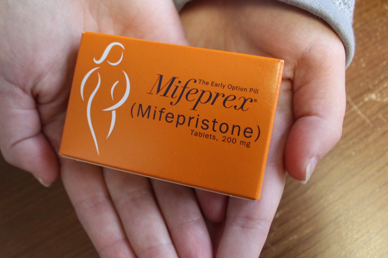 A set of hands holding an orange box of Mifeprex, the name brand of mifepristone