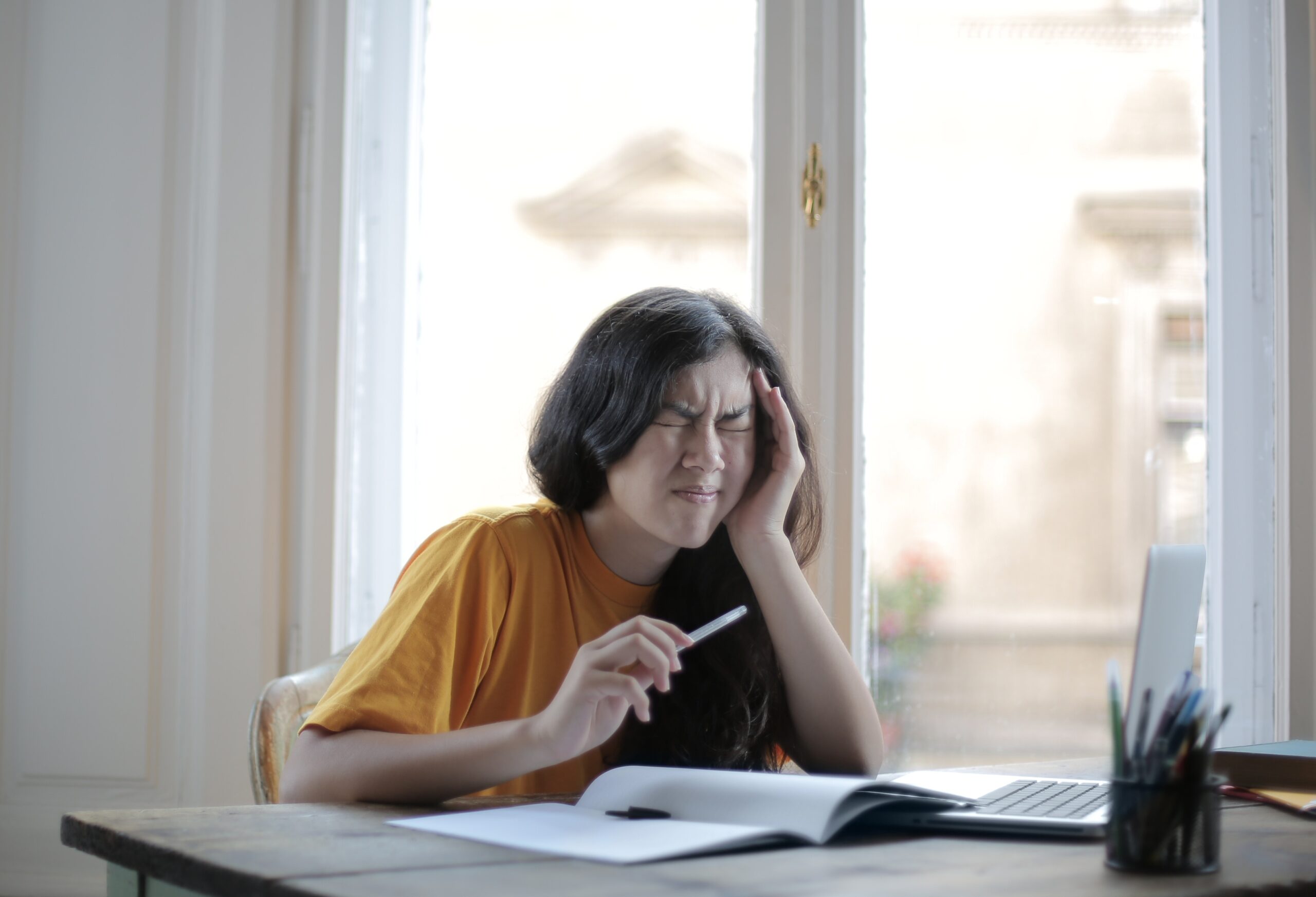 A woman grimaces in pain while sitting at a table with a book open in front of her.