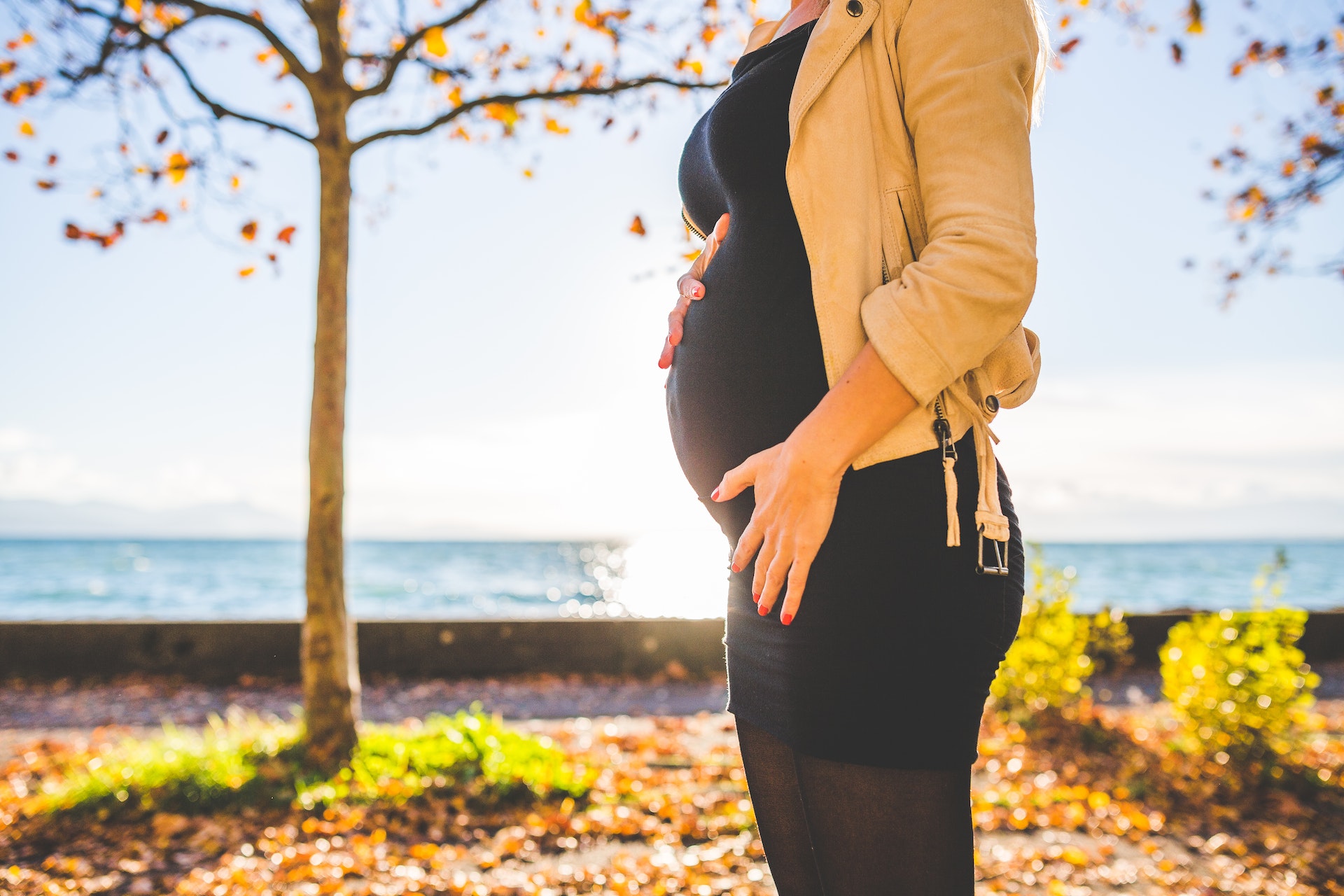 Pregnant person wearing beige jacket standing outside