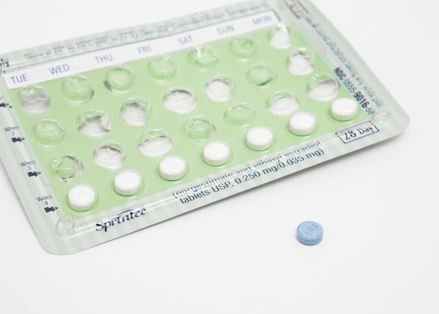 A pack of birth control pills on a white background. One blue pill is in front of the pack