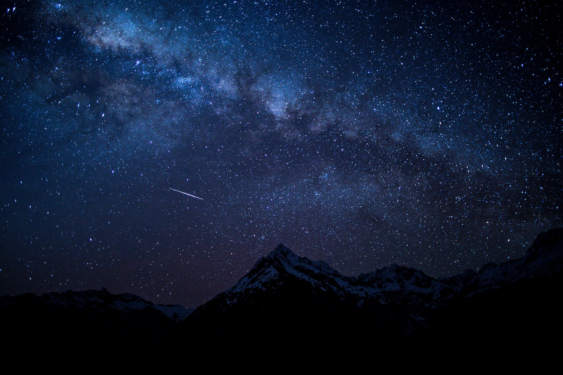 Nightscape of the silhouette of a mountain in New Zealand with the stars, milky way and a comet in the background.