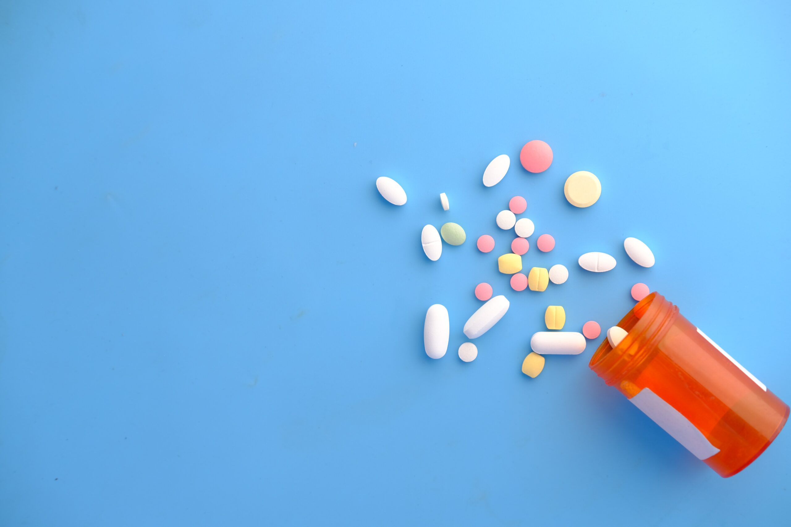 An image showing pills of different colors and sizes spilling out of a plastic pill container