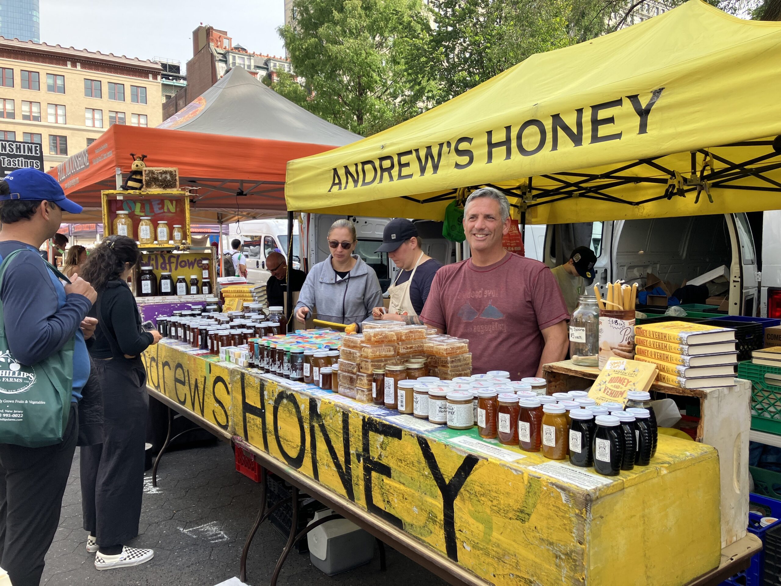 Andrew Coté, a NYC-based beekeeper, stands at his booth at the Union Square Farmers Market. He is surrounded by jars of honey.