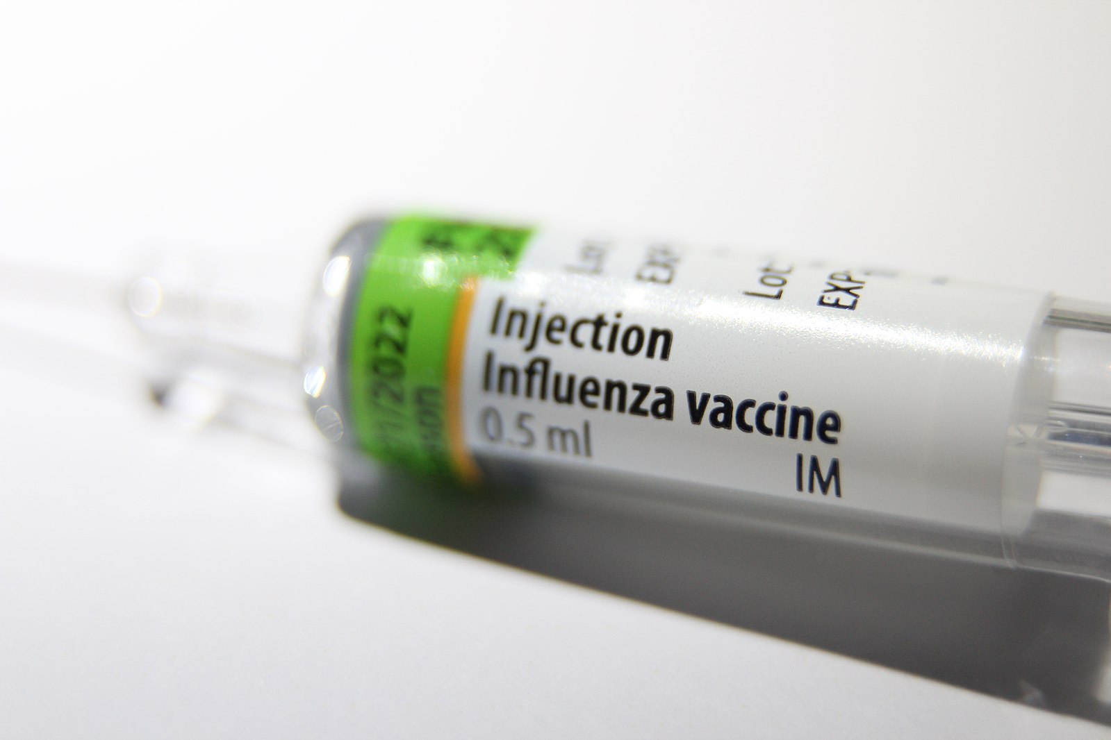 The syringe of an influenza vaccine sits on a white surface.