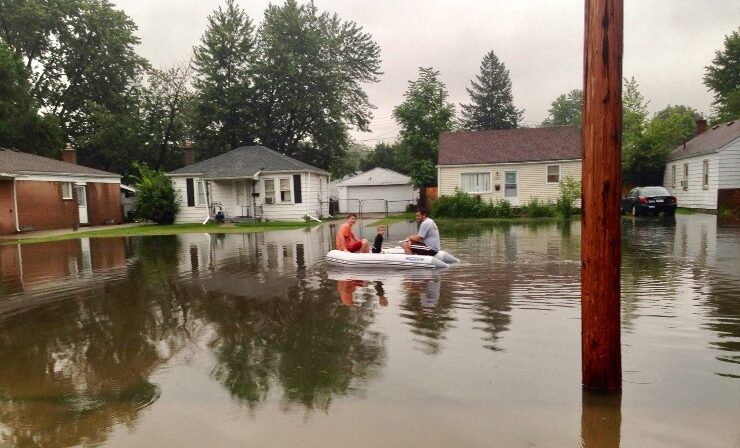 A family of three paddles through flood water on a small raft in southeastern Michigan