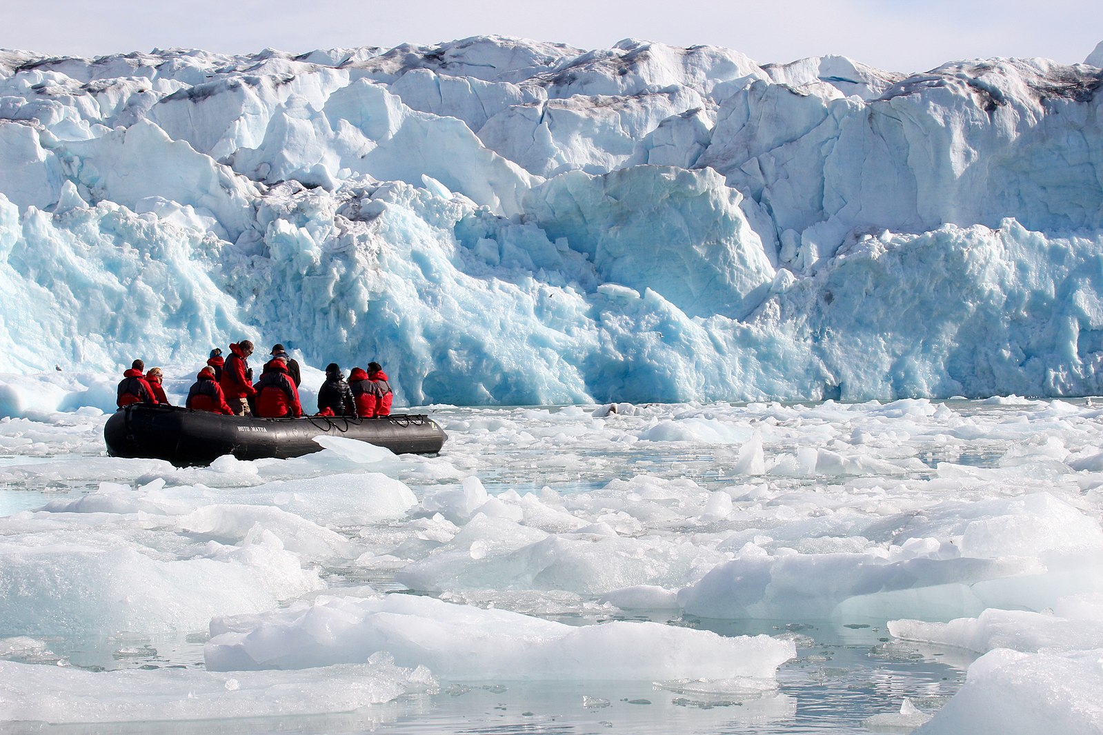 People are on a boat exploring the Arctic, with glaciers in front of them and floating ice all around them