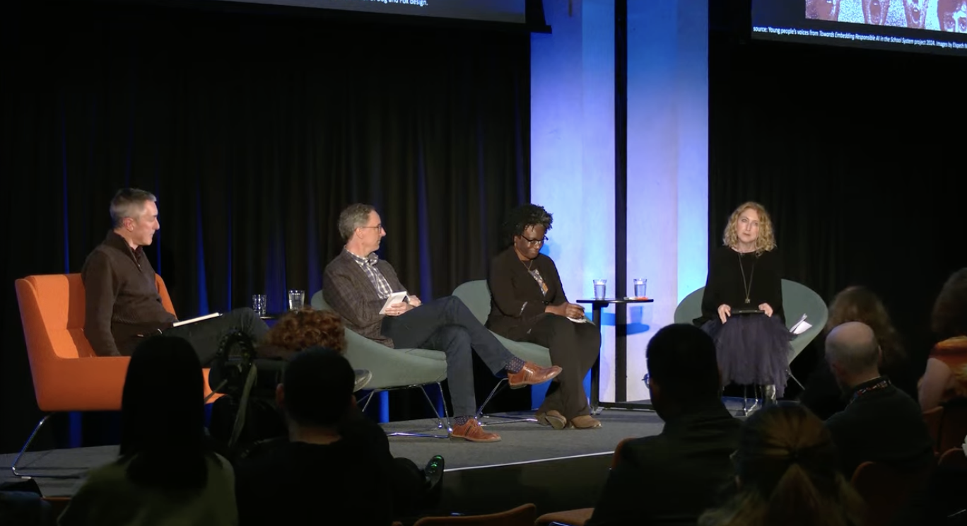 Three panelists and a moderator sit in a dark auditorium, discussing AI in the classroom