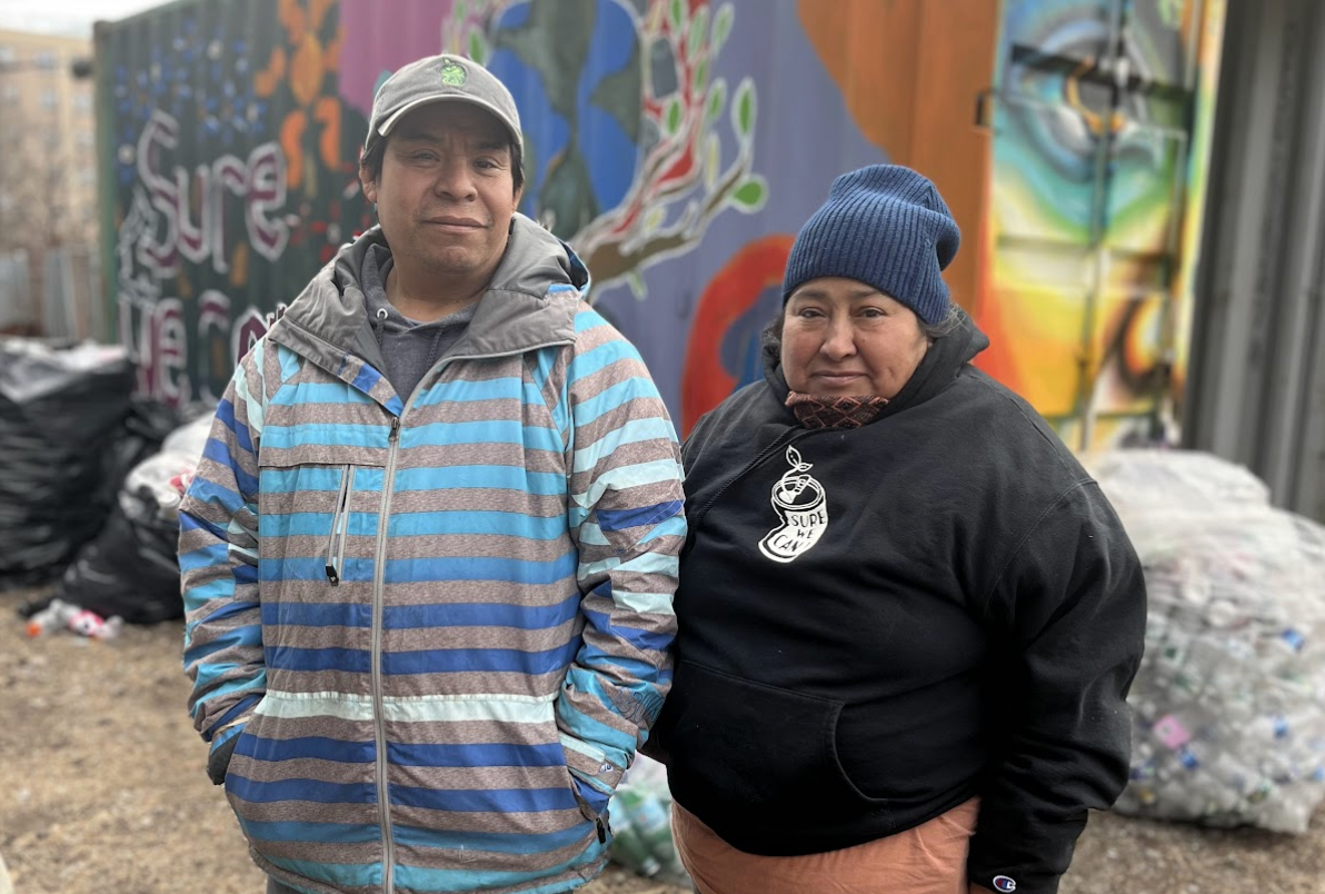 Two can collectors, one man in a grey and blue sweatshirt and one woman in a black sweatshirt, pose in front of an art-covered wall.