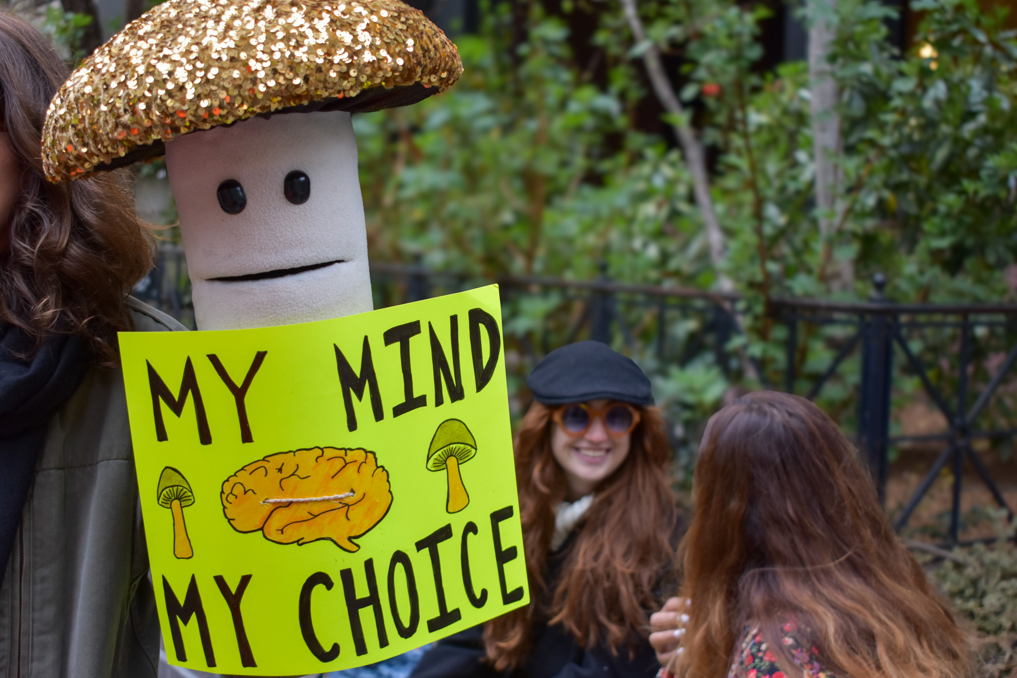 A mushroom puppet at a protest with a sign that reads "my mind my choice". 