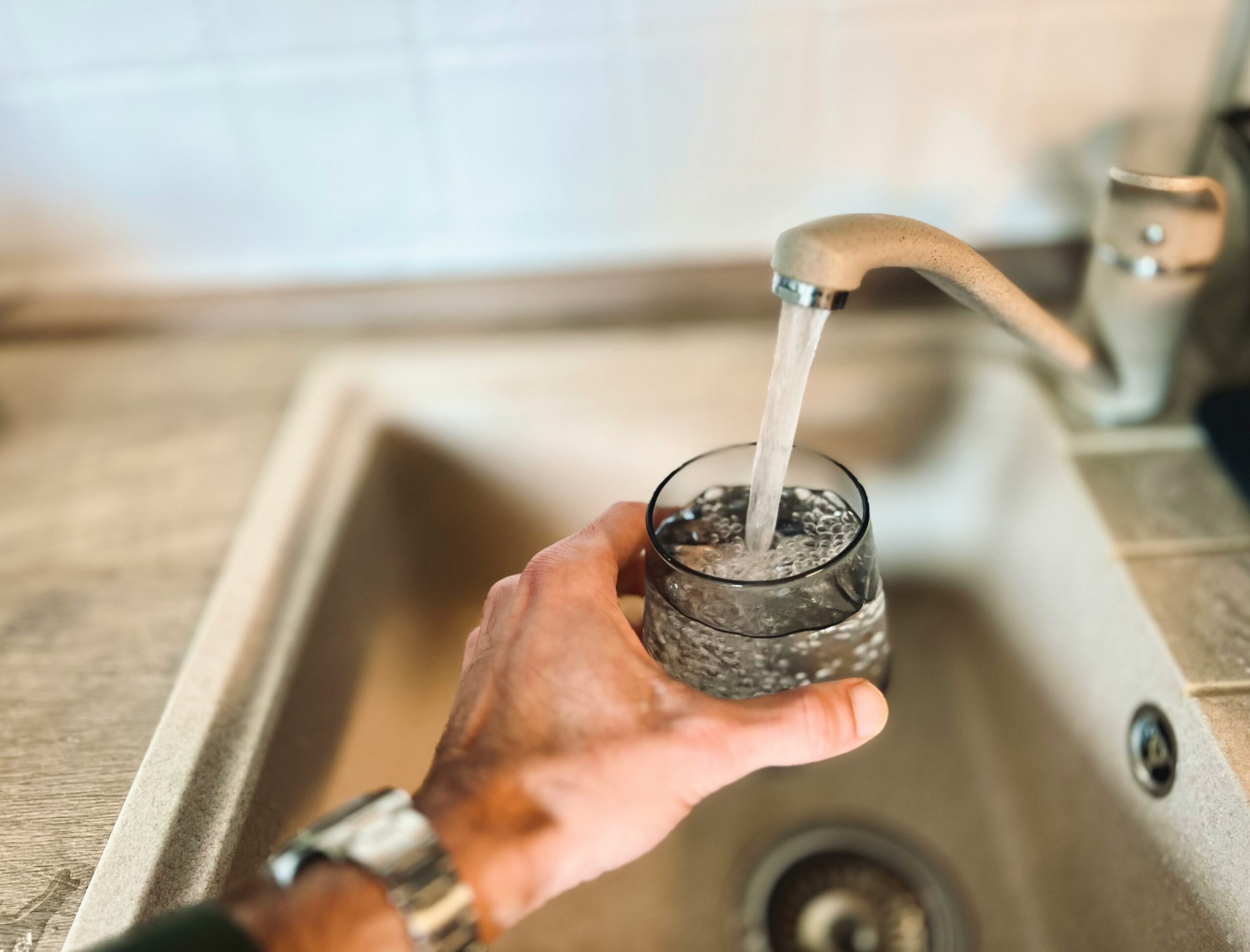 A person pouring water into a glass at a kitchen faucet.
