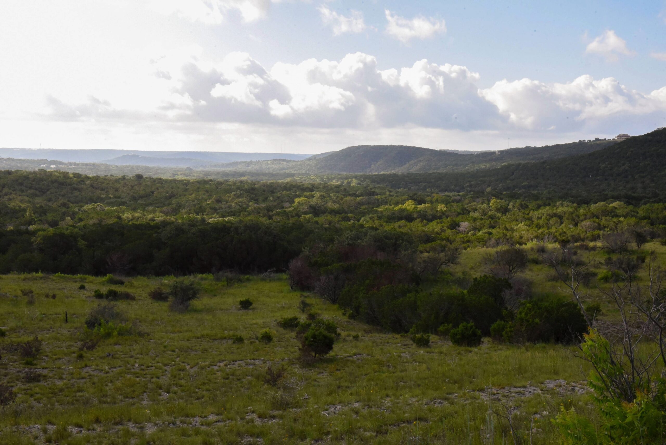 green landscpae of mountains on the right of the screen and valleys below and a blue sky with clouds all across it