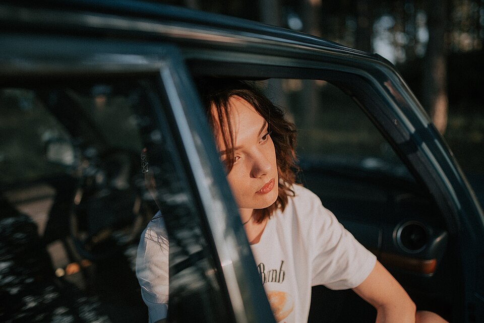 A young woman leans out of a car looking wistful.